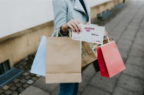 frau hält viele Taschen in der Hand und einen Gutschein