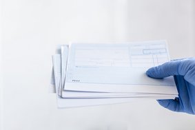 Blaues Rezept wird von blauem Handschuh in die Kamera gehalten